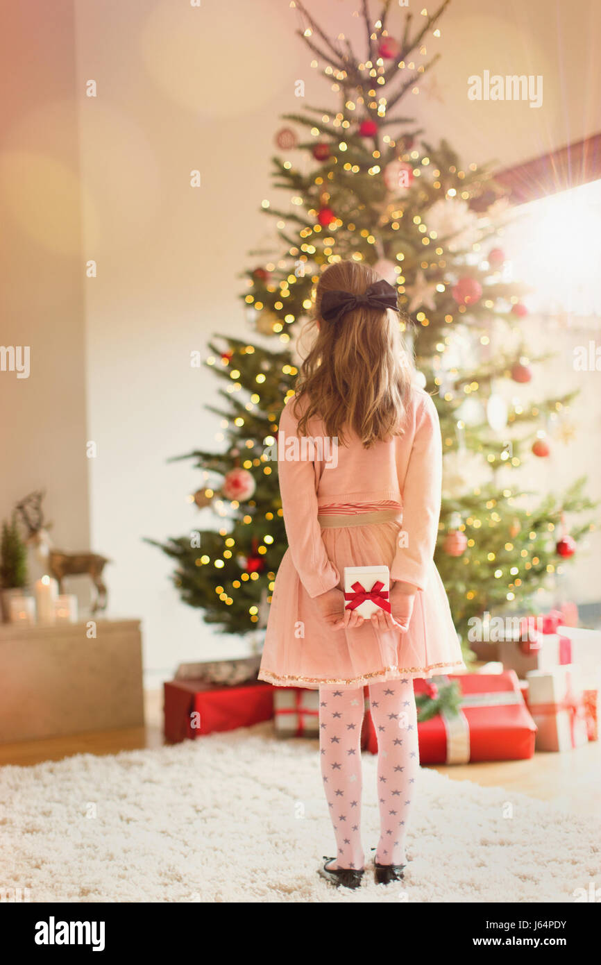 Girl in pink dress holding Christmas gift in front of Christmas tree Stock Photo