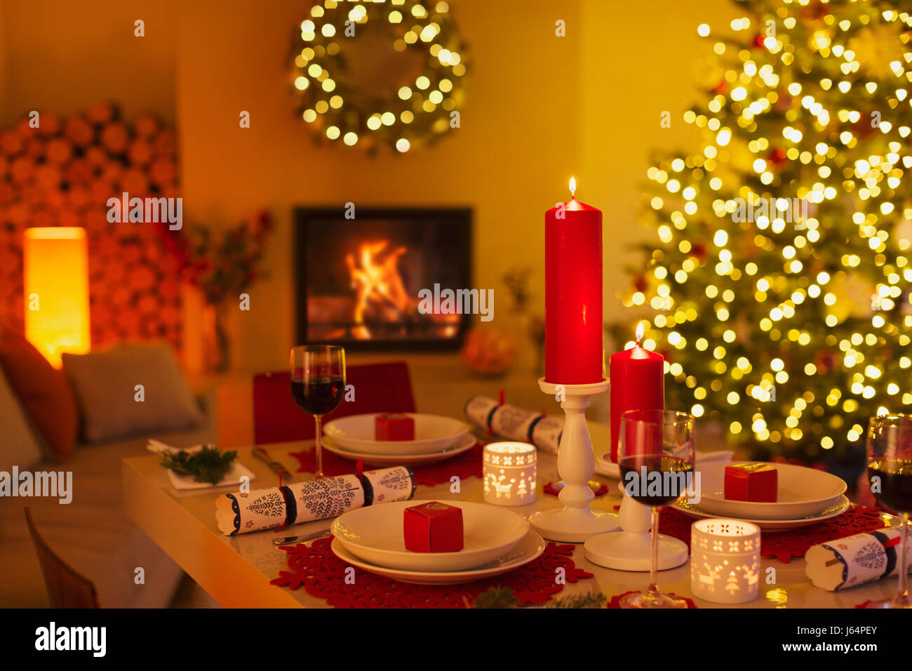 Ambient candles and Christmas crackers on dinner table in living room with fireplace and Christmas tree Stock Photo