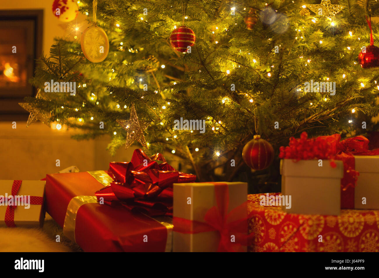Gifts with red bows under illuminated Christmas tree Stock Photo