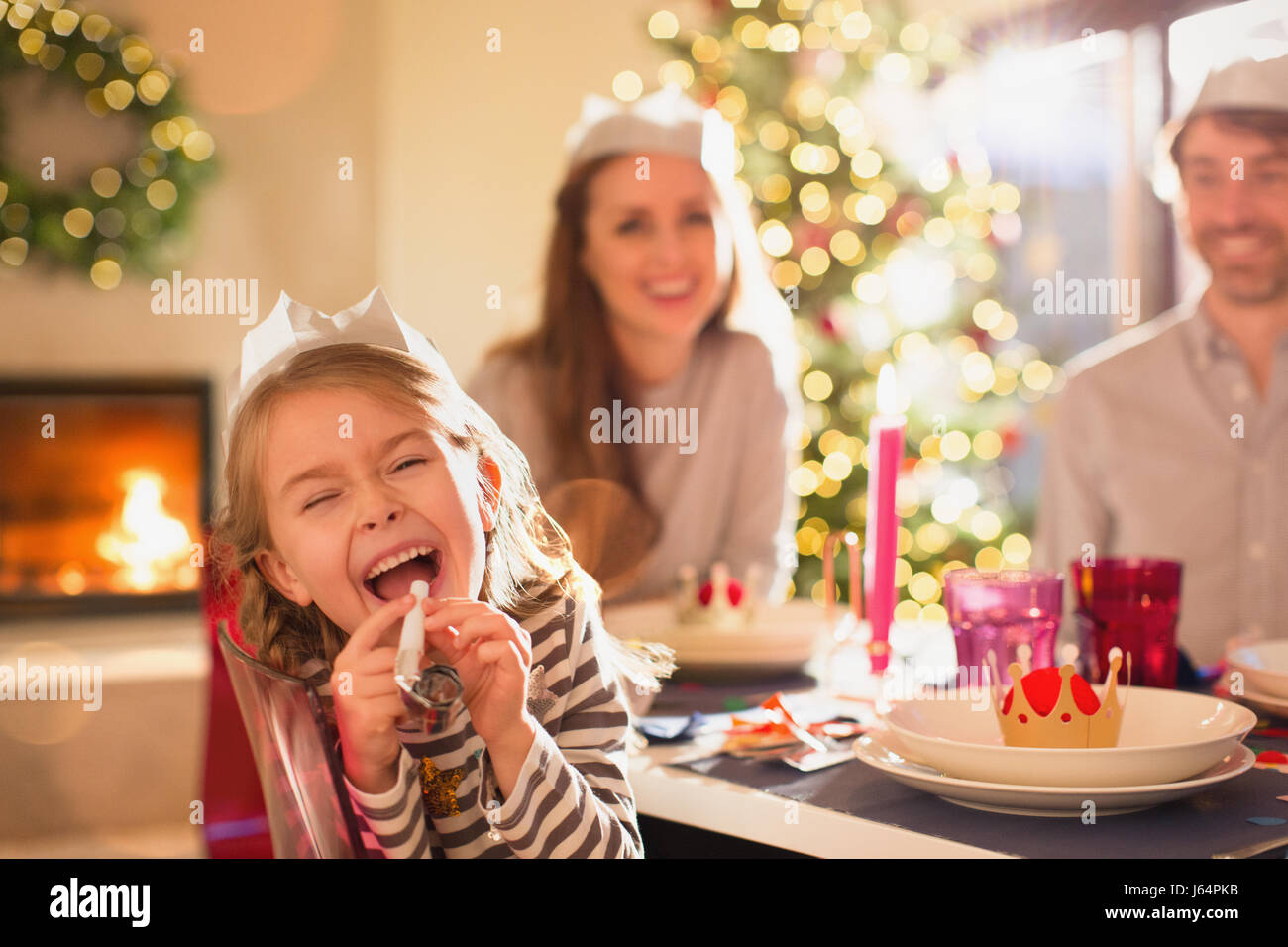Portrait playful girl in paper crown blowing party favor at Christmas dinner table Stock Photo