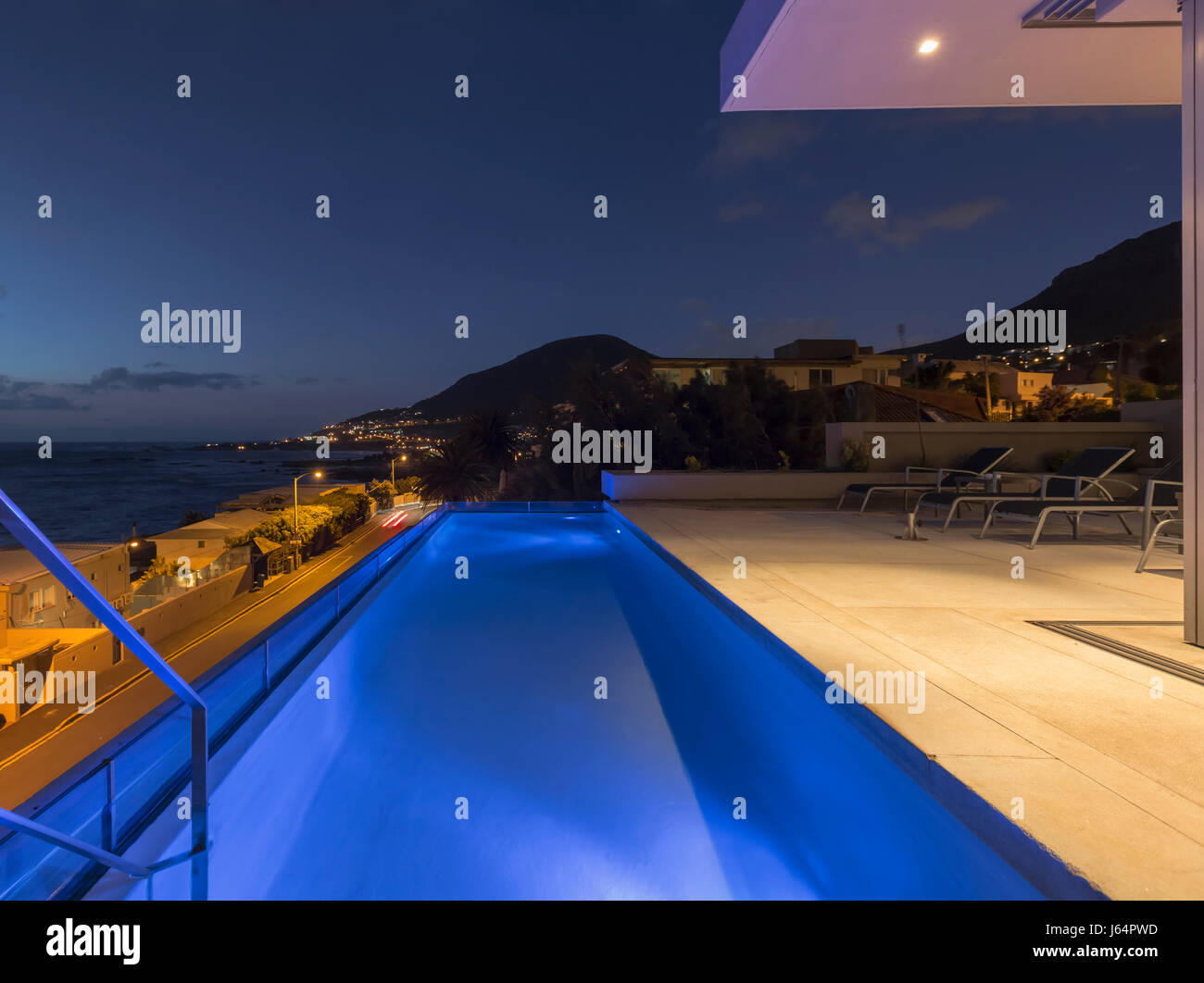 Illuminated blue lap swimming pool on luxury patio at night Stock Photo