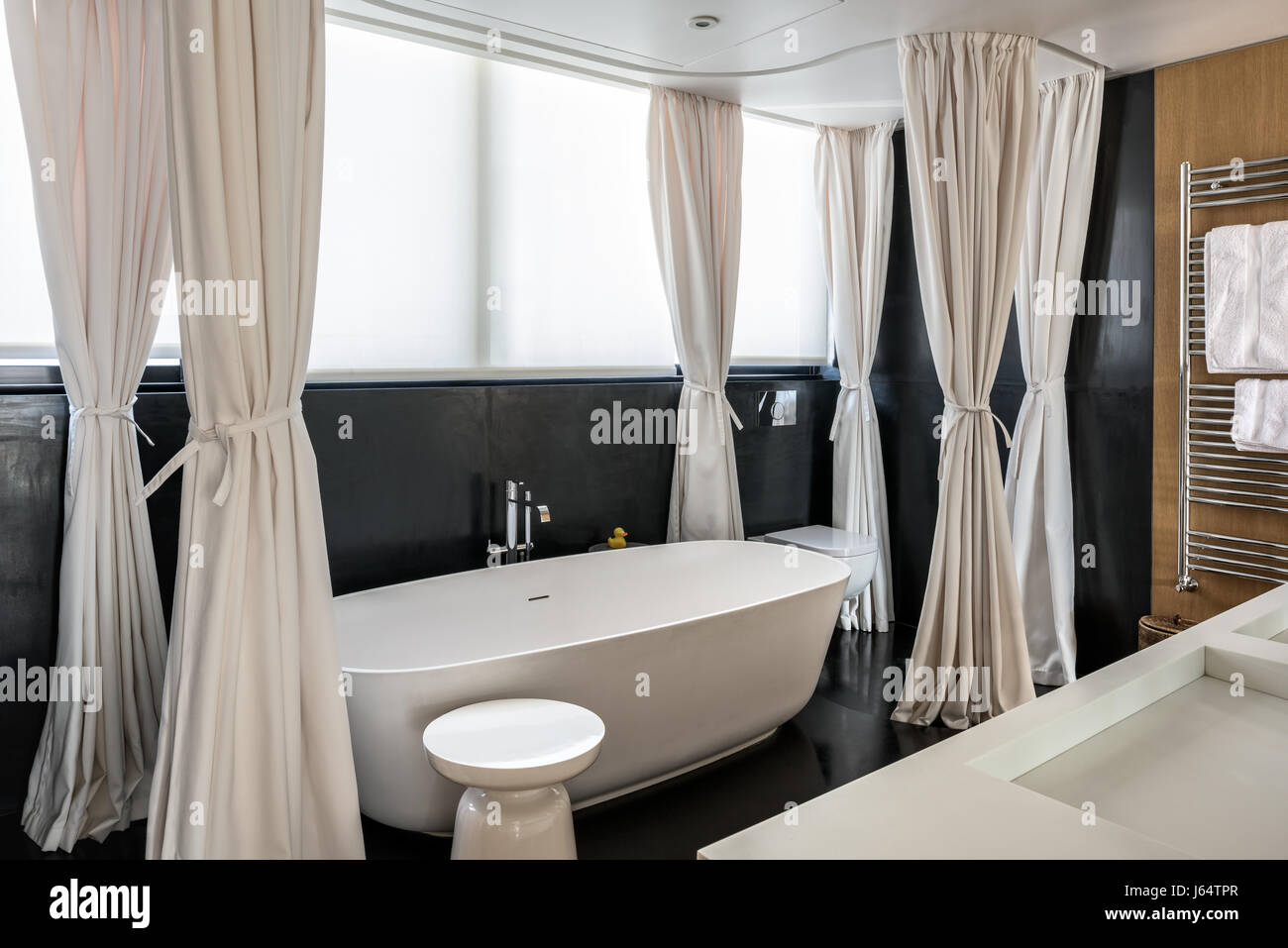 Heavy canvas curtains enclosing bath and shower set in dark honed stone. The basin and bath designer is Antonio Lupi Stock Photo