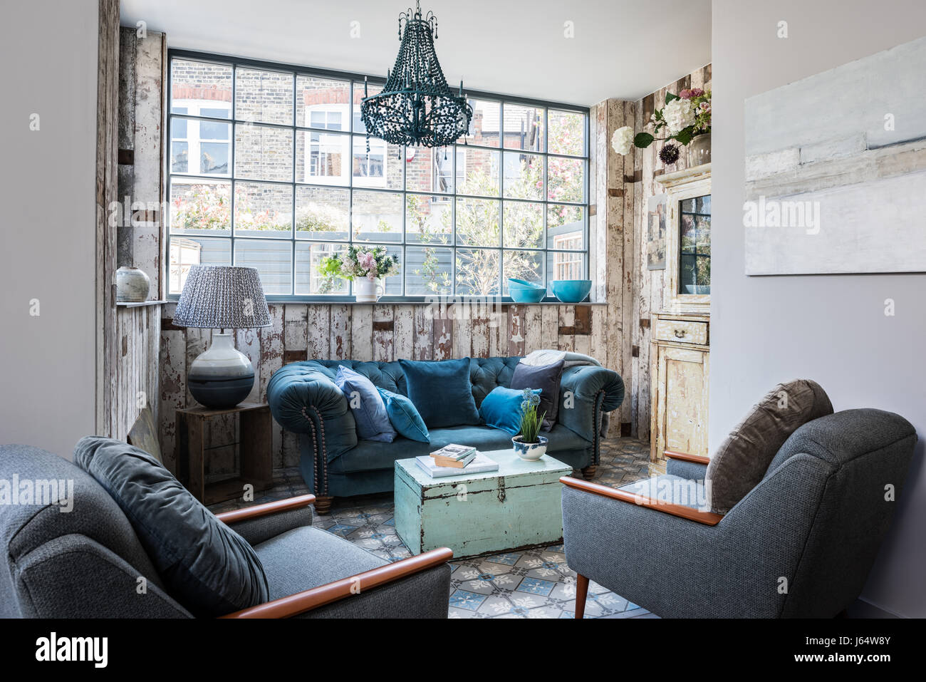 Mid-century armchairs and velvet Chesterfield sofa in sitting room with salvaged wood wall cladding and beaded chandelier Stock Photo