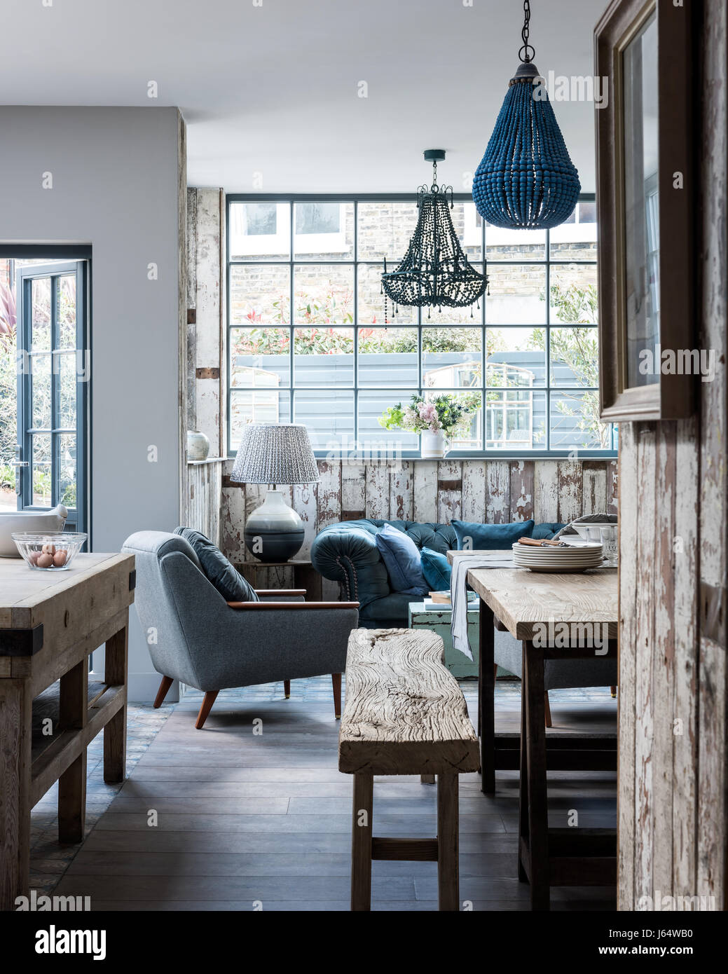 Open plan kitchen diner with mismatching beaded chandeliers, rustic bench and mid century armchair. The floors are white-washed oak Stock Photo