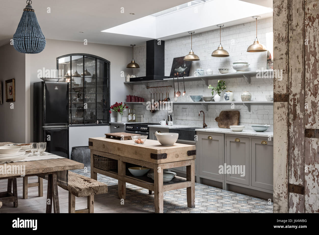 Open plan sophisticaed kitchen with vintage brass pendant lighting, rustic wooden butchers island and beaded chandelier from Graham & Green Stock Photo