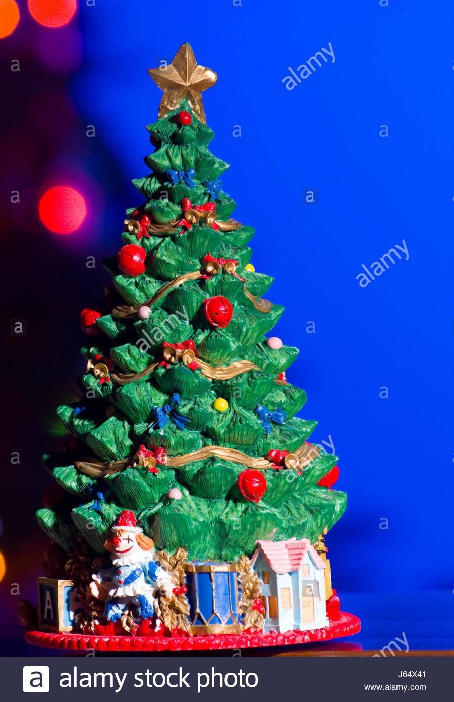 figurine of an evergreen christmas tree and presents set in front of christmas tree with lights - An Evergreen Christmas figurine of an evergreen christmas tree and presents set in front of christmas tree with lights - An Evergreen Christmas
