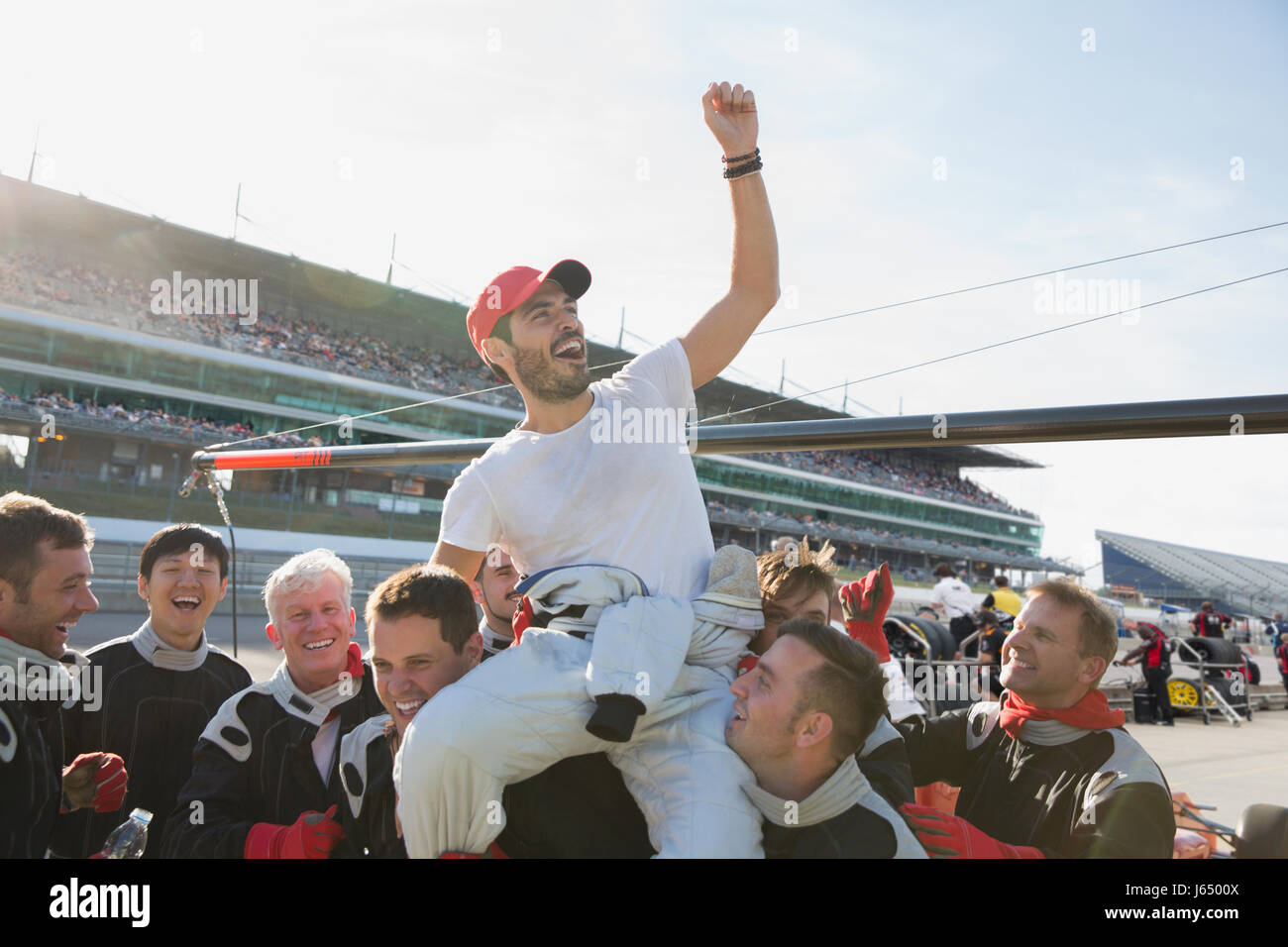 Formula one racing team carrying cheering driver on shoulders, celebrating victory on sports track Stock Photo