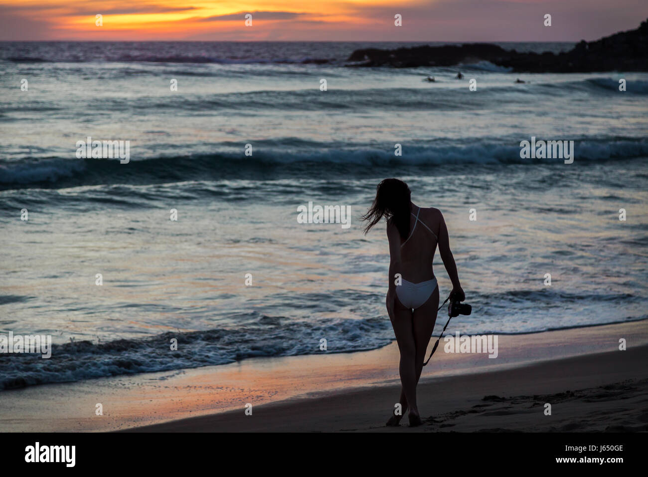 Pretty young woman on a beach at sunset with a camera in her hand. Stock Photo