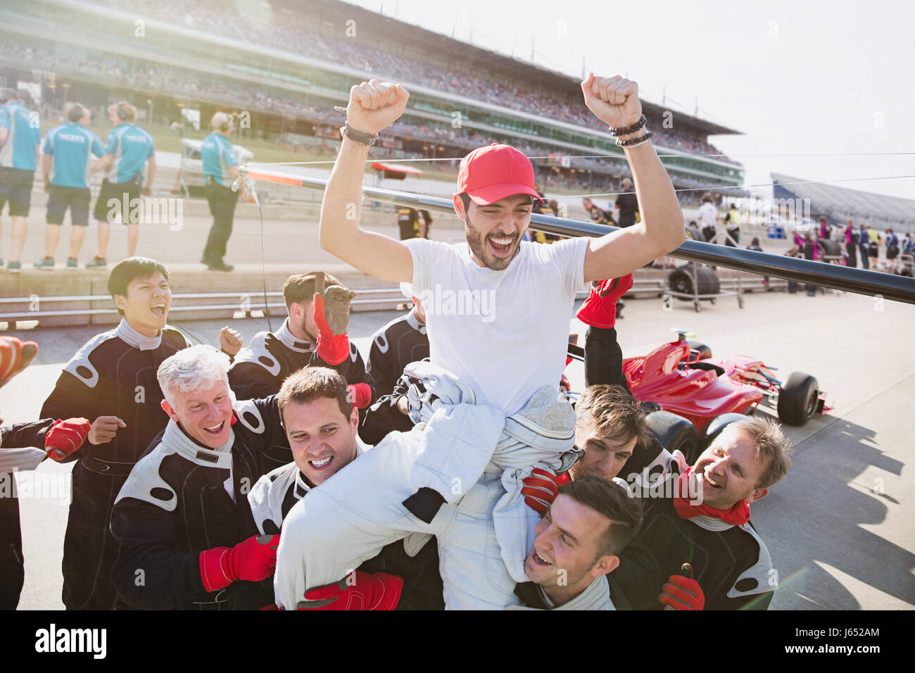 Formula one racing team carrying driver on shoulders, celebrating victory on sports track Stock Photo