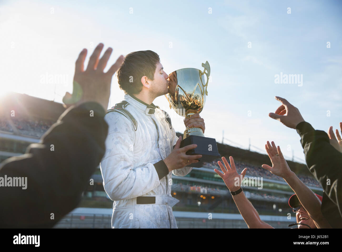 Formula one racing team cheering around driver kissing trophy, celebrating victory Stock Photo