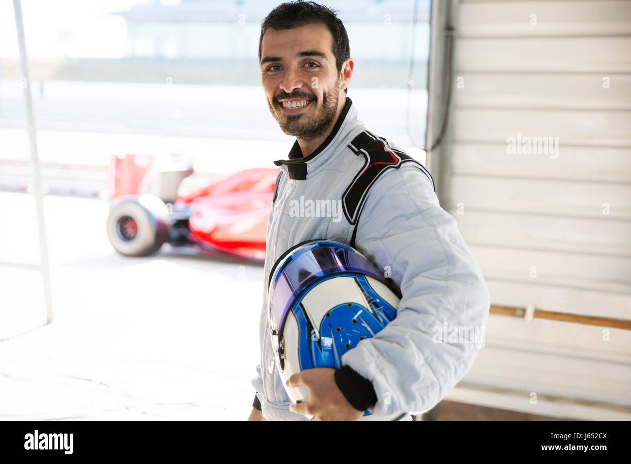 Portrait confident male formula one race car driver holding helmet in repair garage Stock Photo