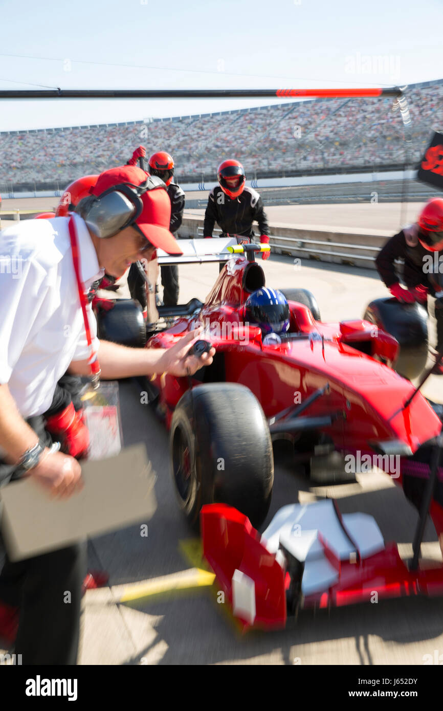 Manager with stopwatch timing pit crew replacing tires on formula one race car in practice session pit lane Stock Photo