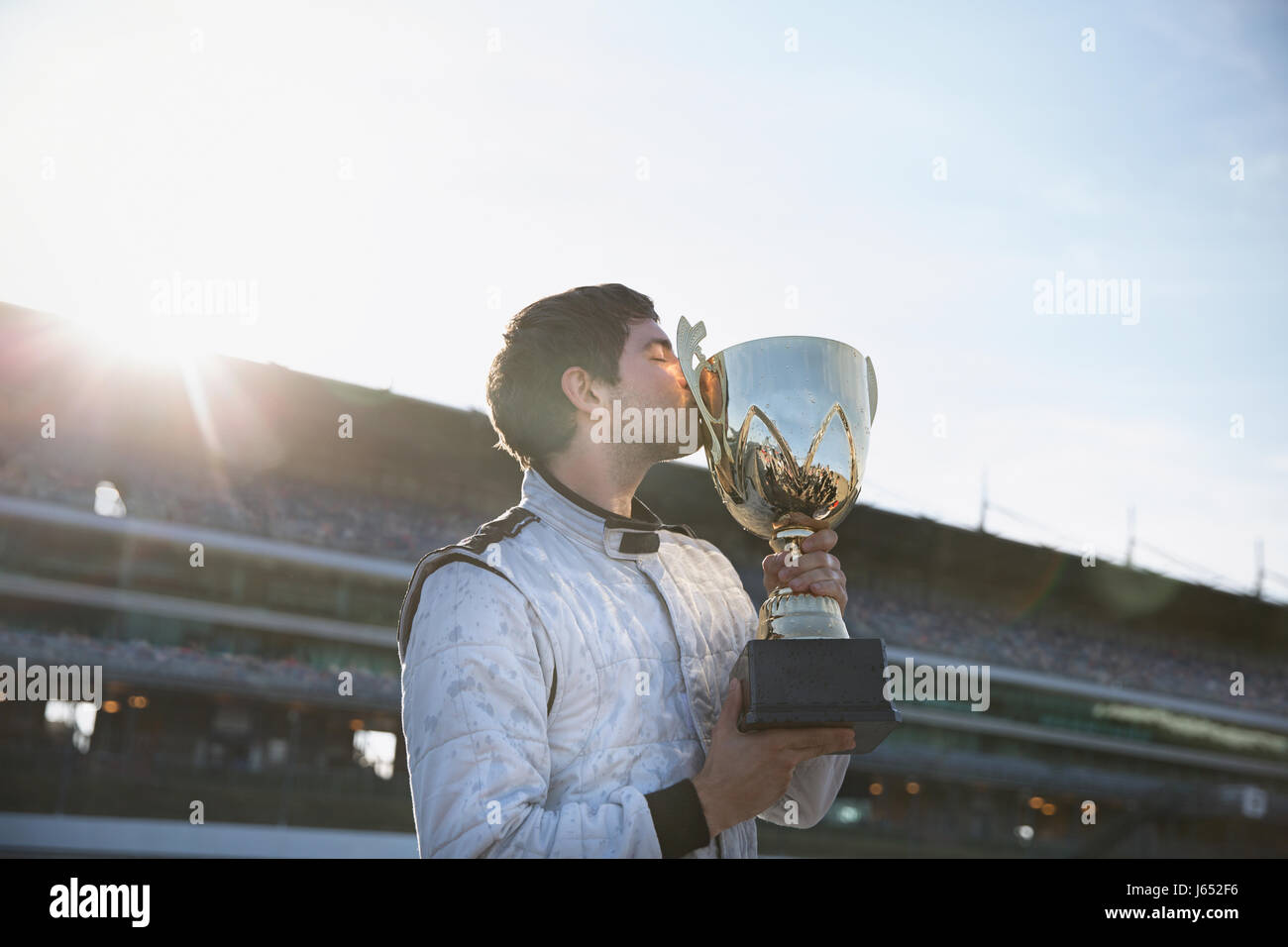 Male formula one driver kissing trophy, celebrating victory on sports track Stock Photo
