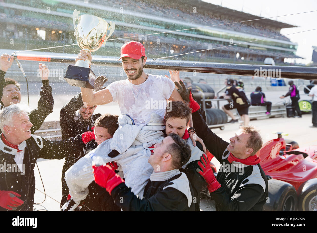Formula one racing team carrying driver with trophy on shoulders, celebrating victory on sports track Stock Photo