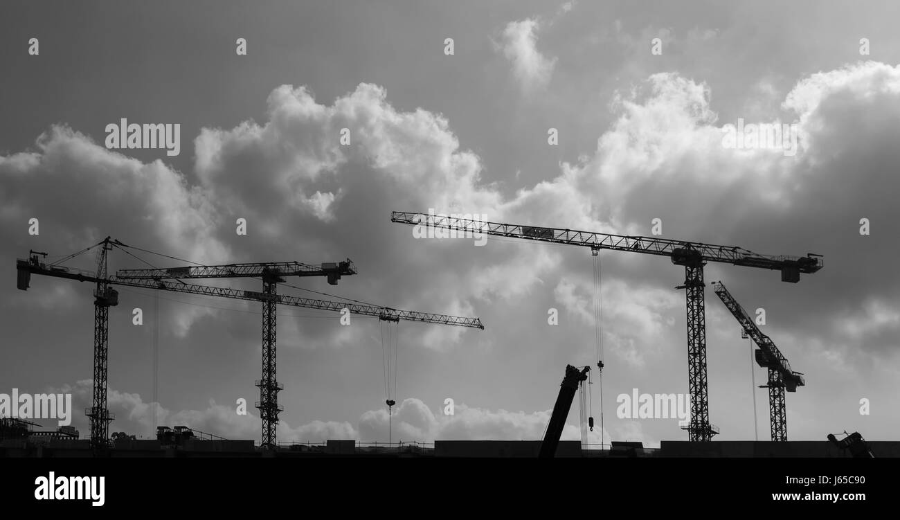 Tower cranes at construction site against cloudy sky Stock Photo - Alamy