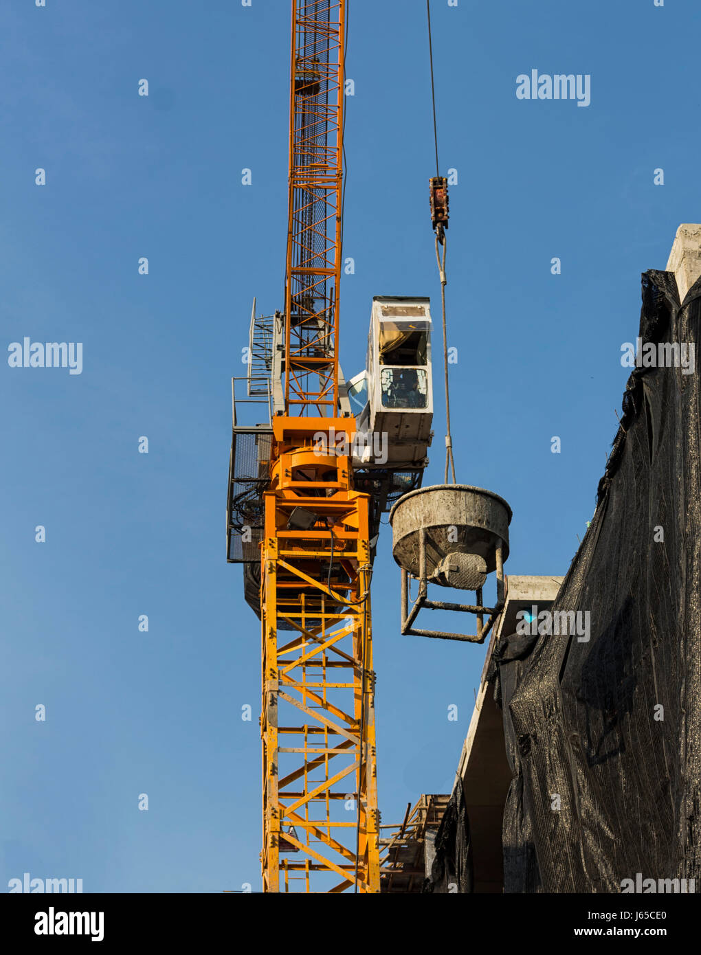 Tower crane lift cement bucket up to top of building during construcion with blue sky background Stock Photo