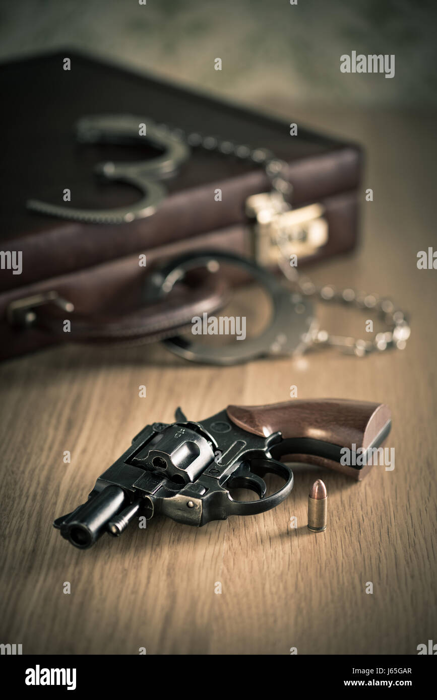 Vintage revolver and bullet with briefcase and handcuffs on background. Stock Photo
