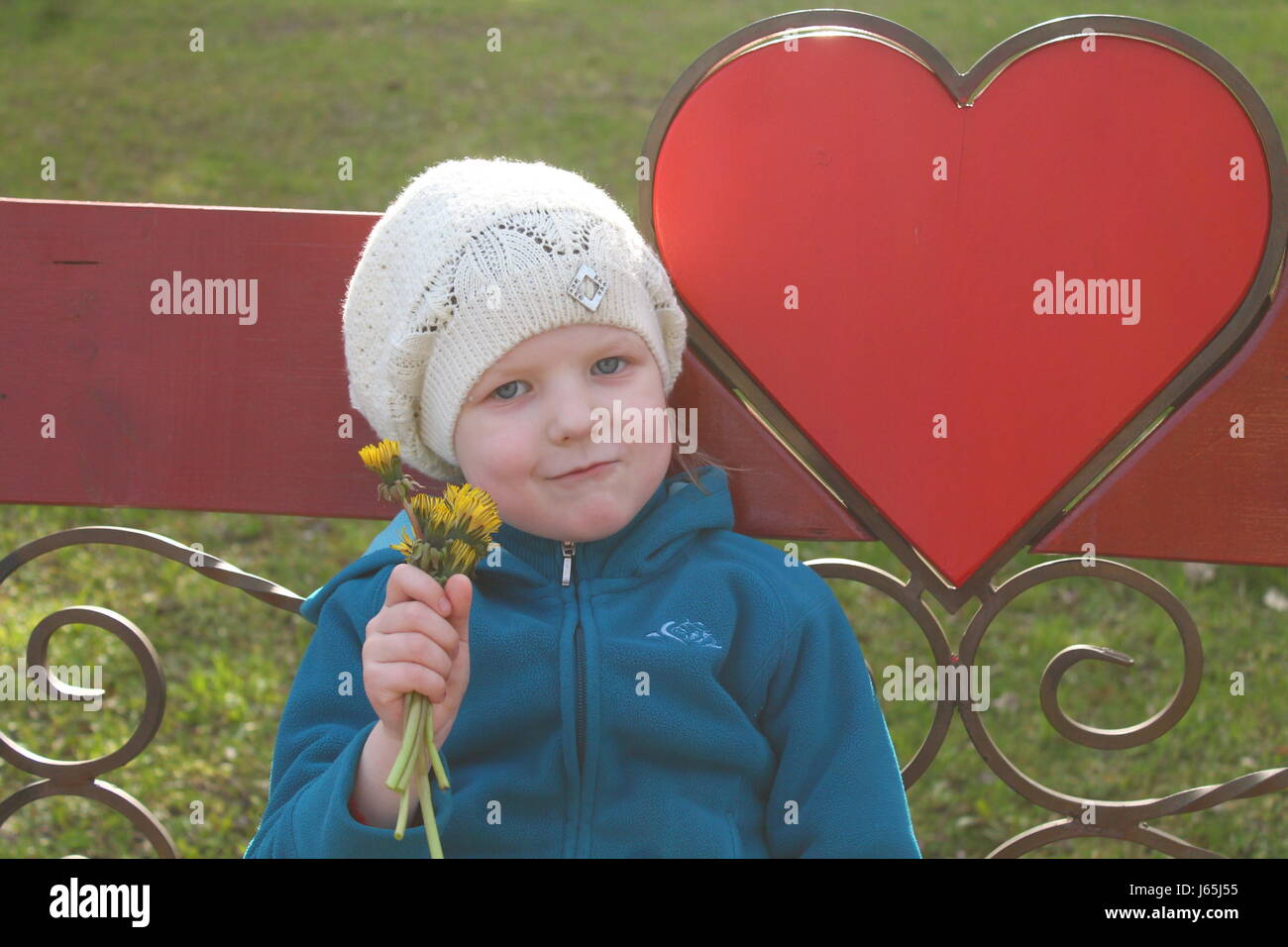 beautiful blonde girl with smiling face with bouquet of yellow dandelion flowers rest under red heart send all love and peace Stock Photo