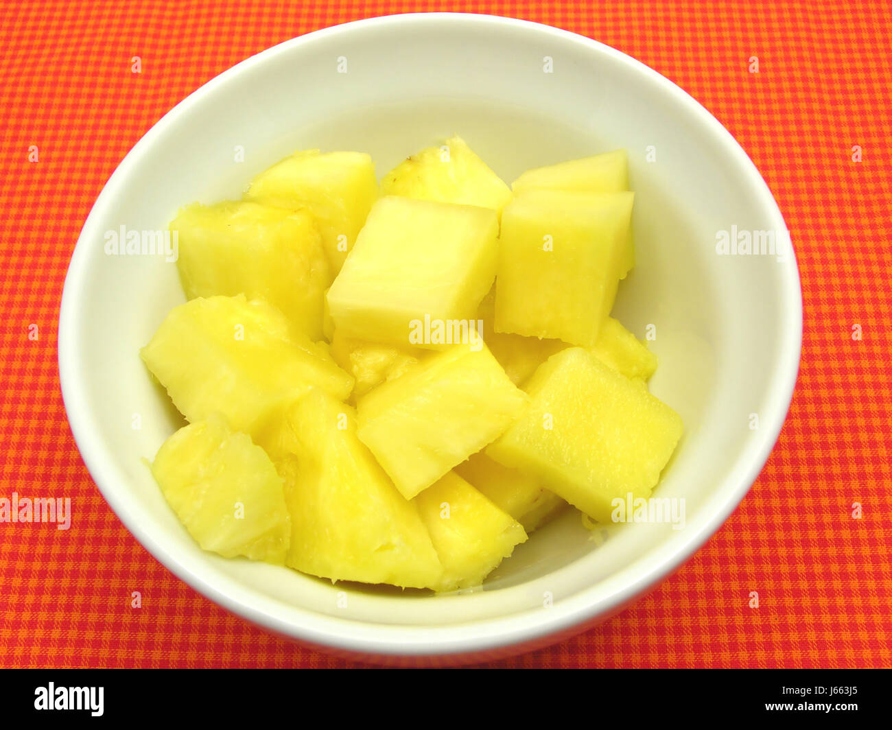 pineapple chunks in a white china bowl on red-checkered pad Stock Photo