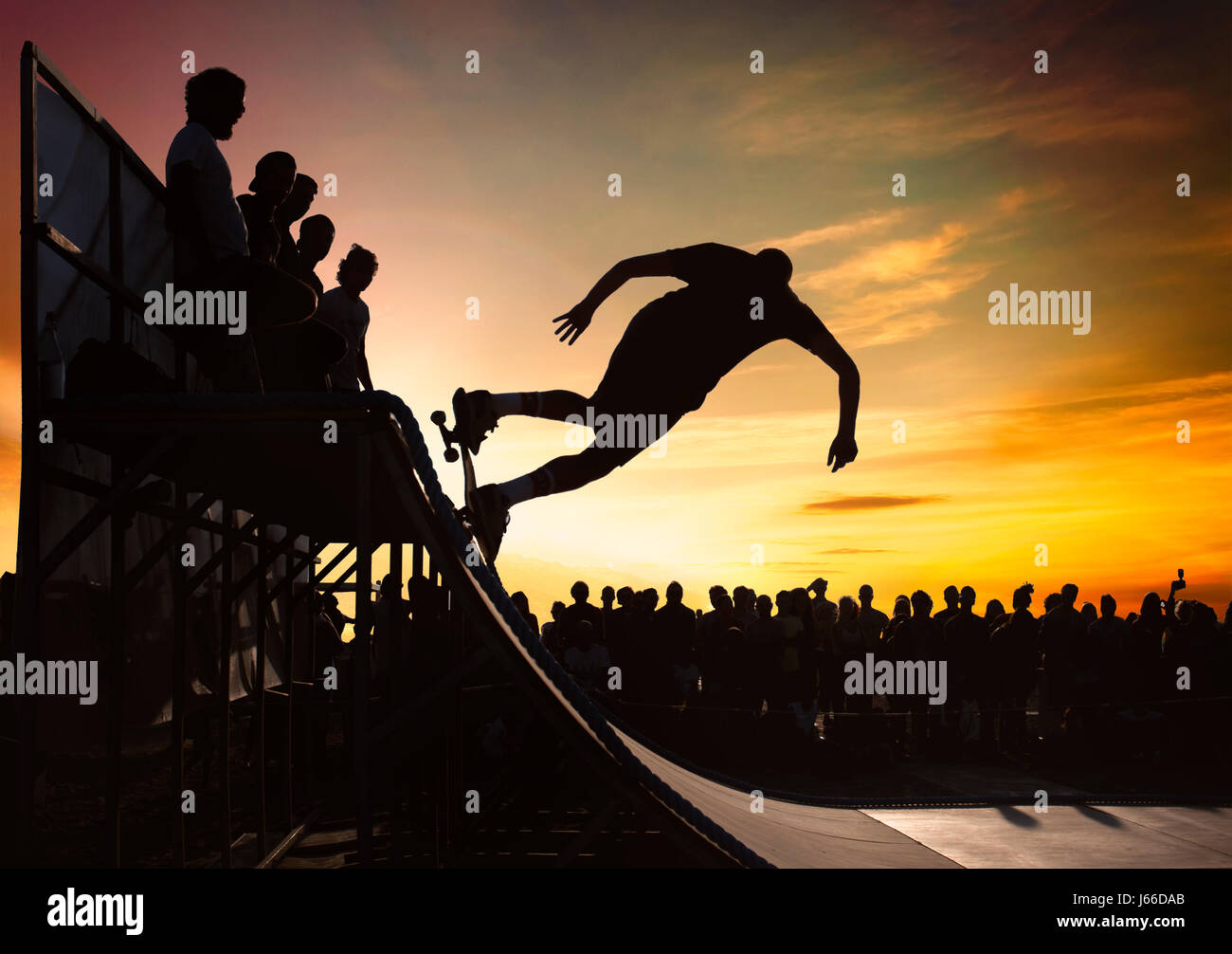 Young man skating on a ramp on sunset with crowd. Stock Photo