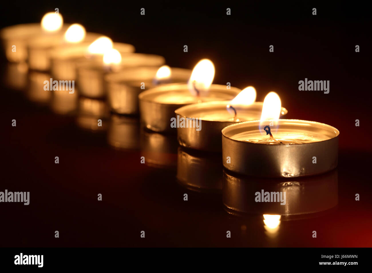 Set of lighting candles in a row on dark background with reflection
