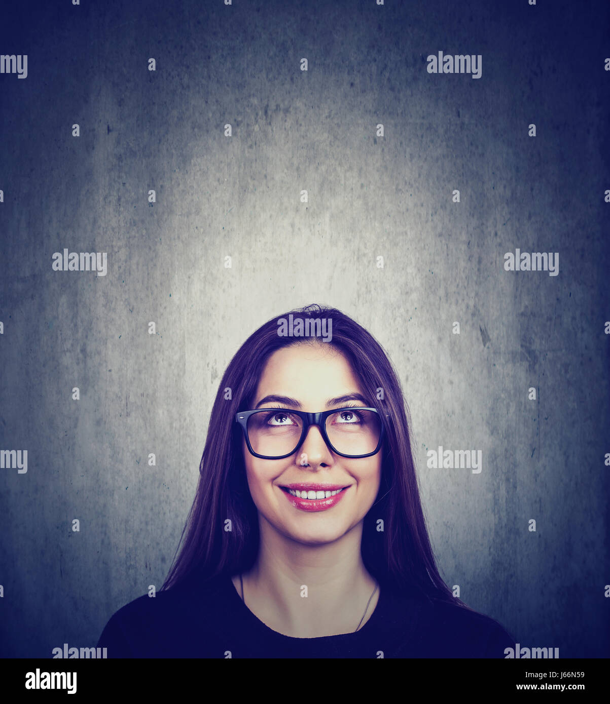 Portrait of an attractive young brunette thoughtful woman smiling looking up isolated on gray grunge wall background Stock Photo