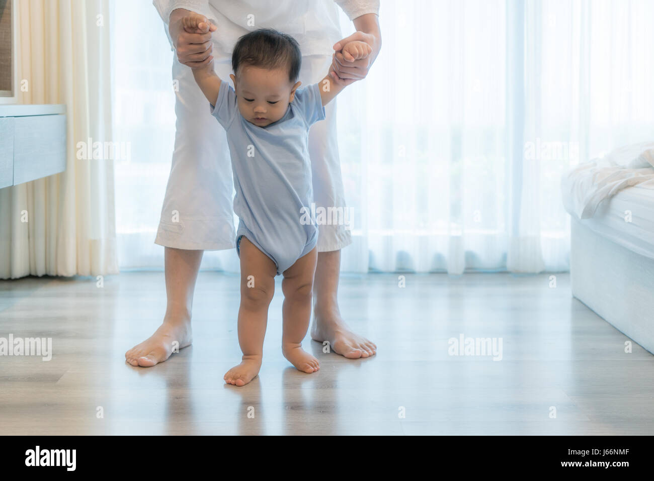 Happy Asian little baby boy learning to walk with mother help in bedroom at home. Family, child, childhood and parenthood concept Stock Photo