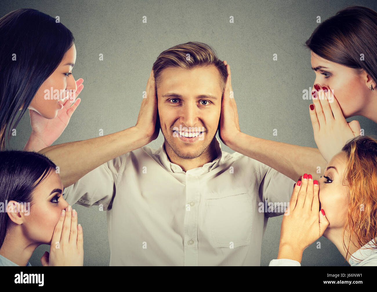 Four women whispering a secret latest gossip to a happy young man who covers ears and ignoring all surrounding noise Stock Photo