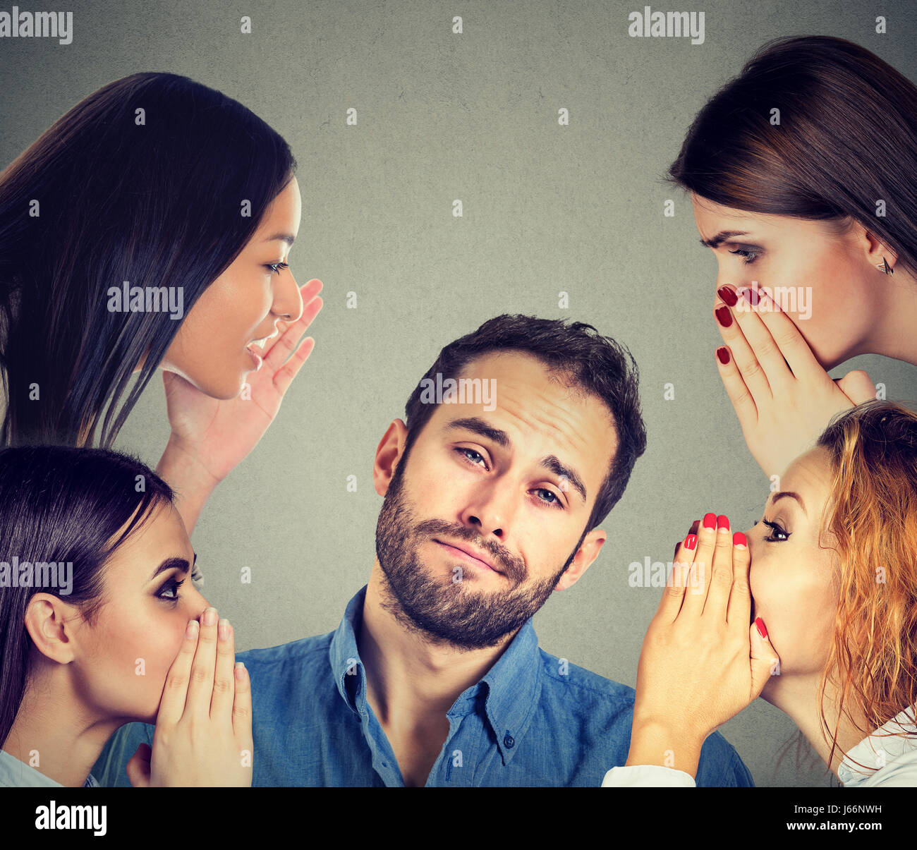 Four women whispering a secret latest gossip to a bored annoyed man Stock Photo