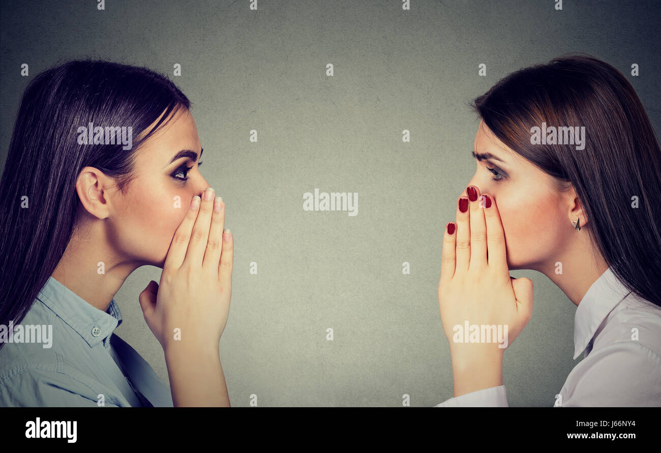 Two women whispering a gossip secret to each other isolated on gray ...