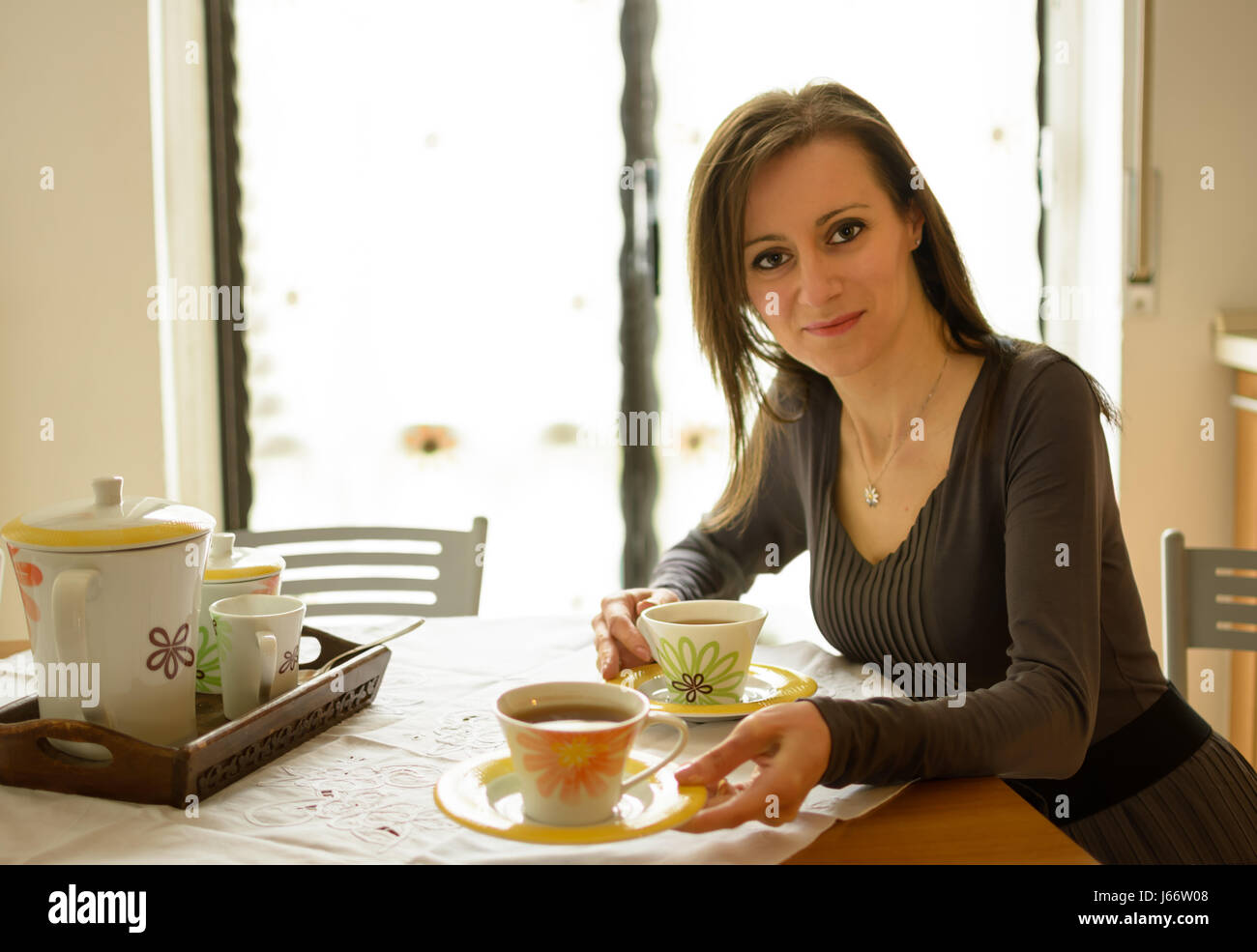 Woman sitting at table offering a cup of tea Stock Photo