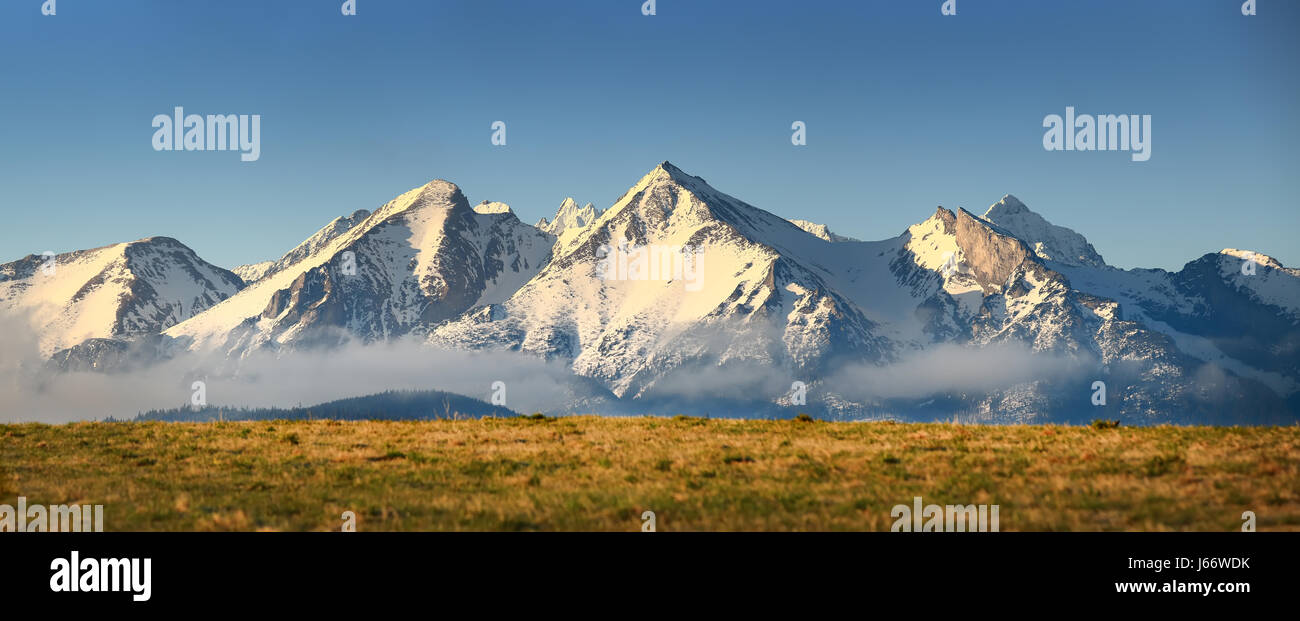 Snowy mountains peaks on blue sky background. Clear blue sky over snowy Alps. Panoramic mountain landscape. Stock Photo