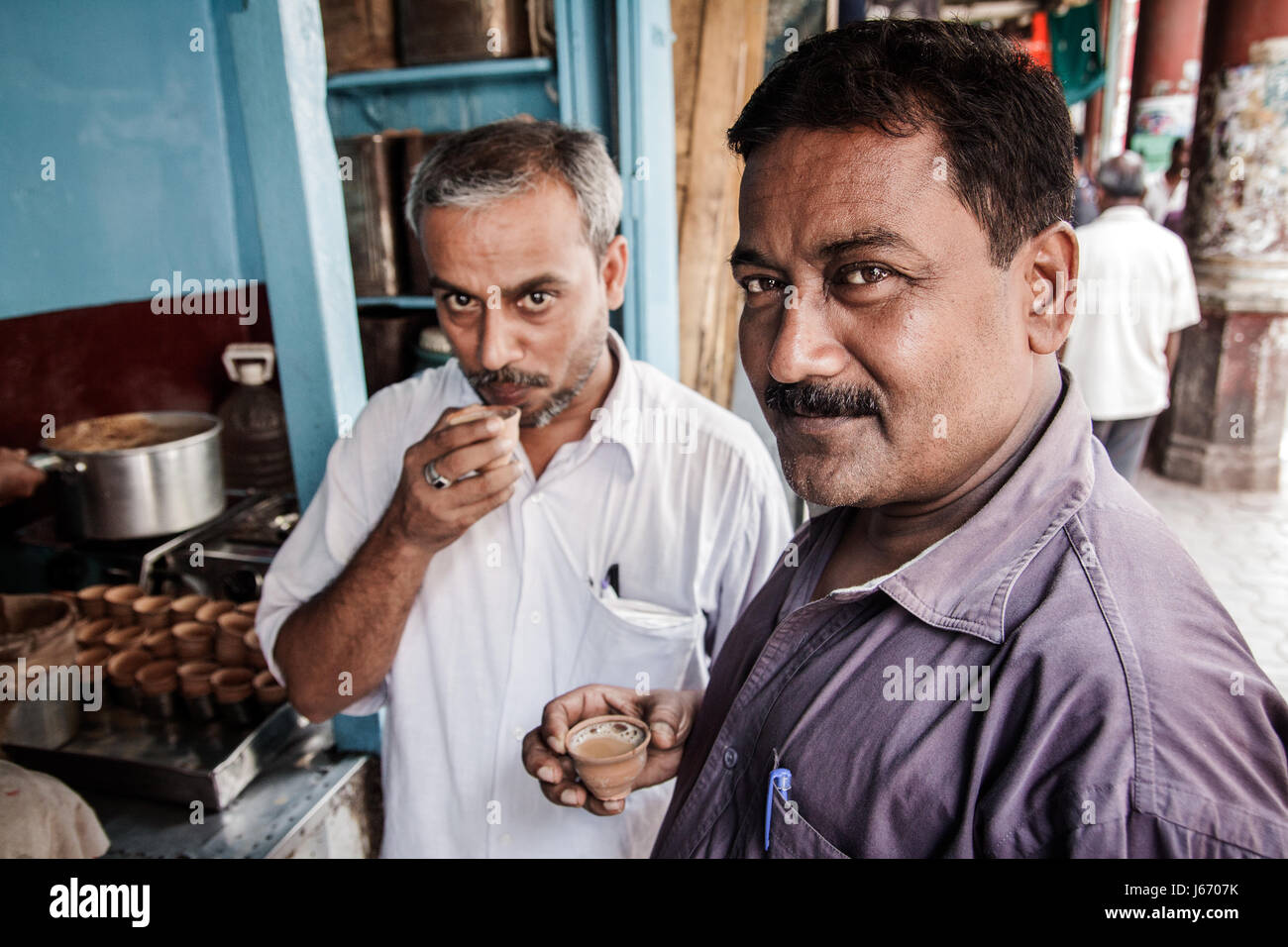 Two men of Indian ethnicity drink Indian tea or Chai as it is known on the subcontinent from traditional clay cups in a tea shop in Kolkata, India Stock Photo