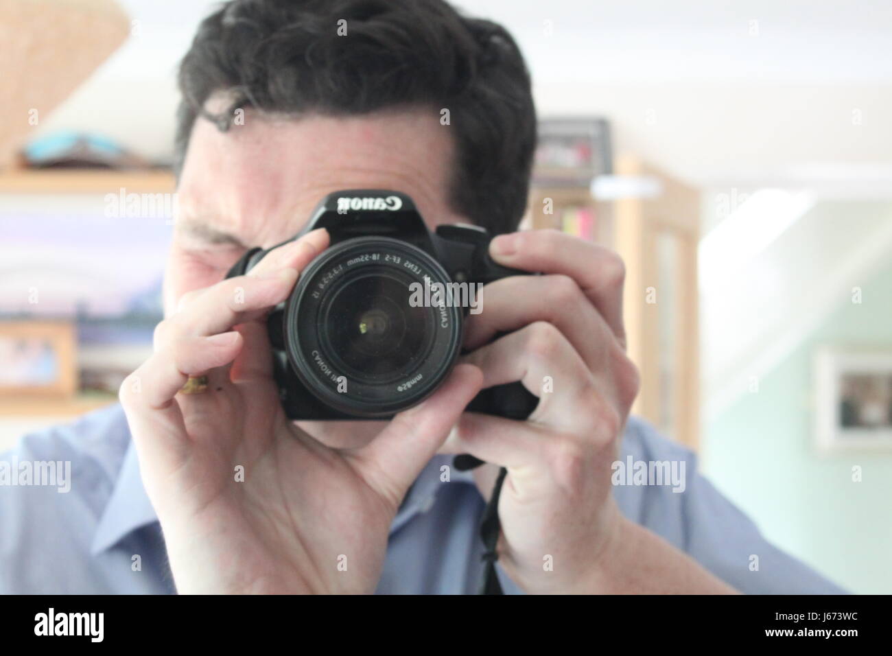 Man with black hair and blue shirt taking a self portrait photo in a mirror inside a house Stock Photo
