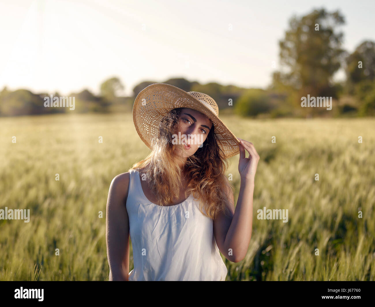 Blonde girl outdoors. With hat and white dress in the wheat field ...