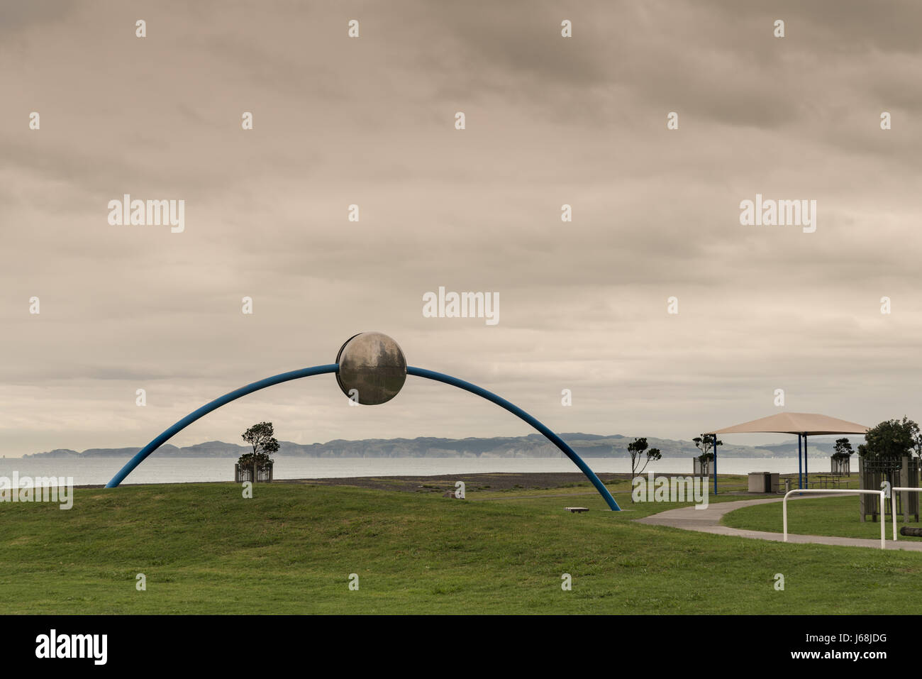 Napier, New Zealand - March 9, 2017: Metal Ecliptic sculpture by David Trubridge at beach park under heavy brown storm sky. Pacific Ocean and green la Stock Photo