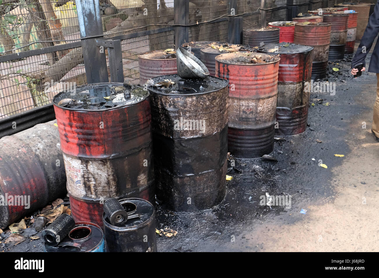 Old rusty barrel left in the road leaking thick black tar or oil on an urban street in Kolkata, India on February 10, 20 Stock Photo