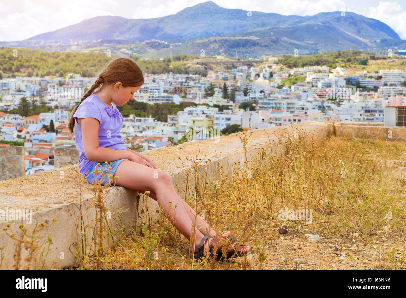 Beautiful teenage girl sitting on background of resort Greek architecture Rethymno city-port, built by Venetians, from height of Fortezza Castle - for Stock Photo