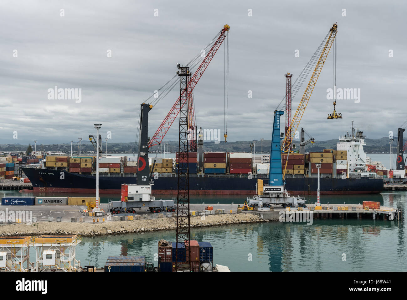 Napier, New Zealand - March 9, 2017: Penelope container ship unloads in the commercial port under heavy skies. Piles of containers, cranes and other h Stock Photo