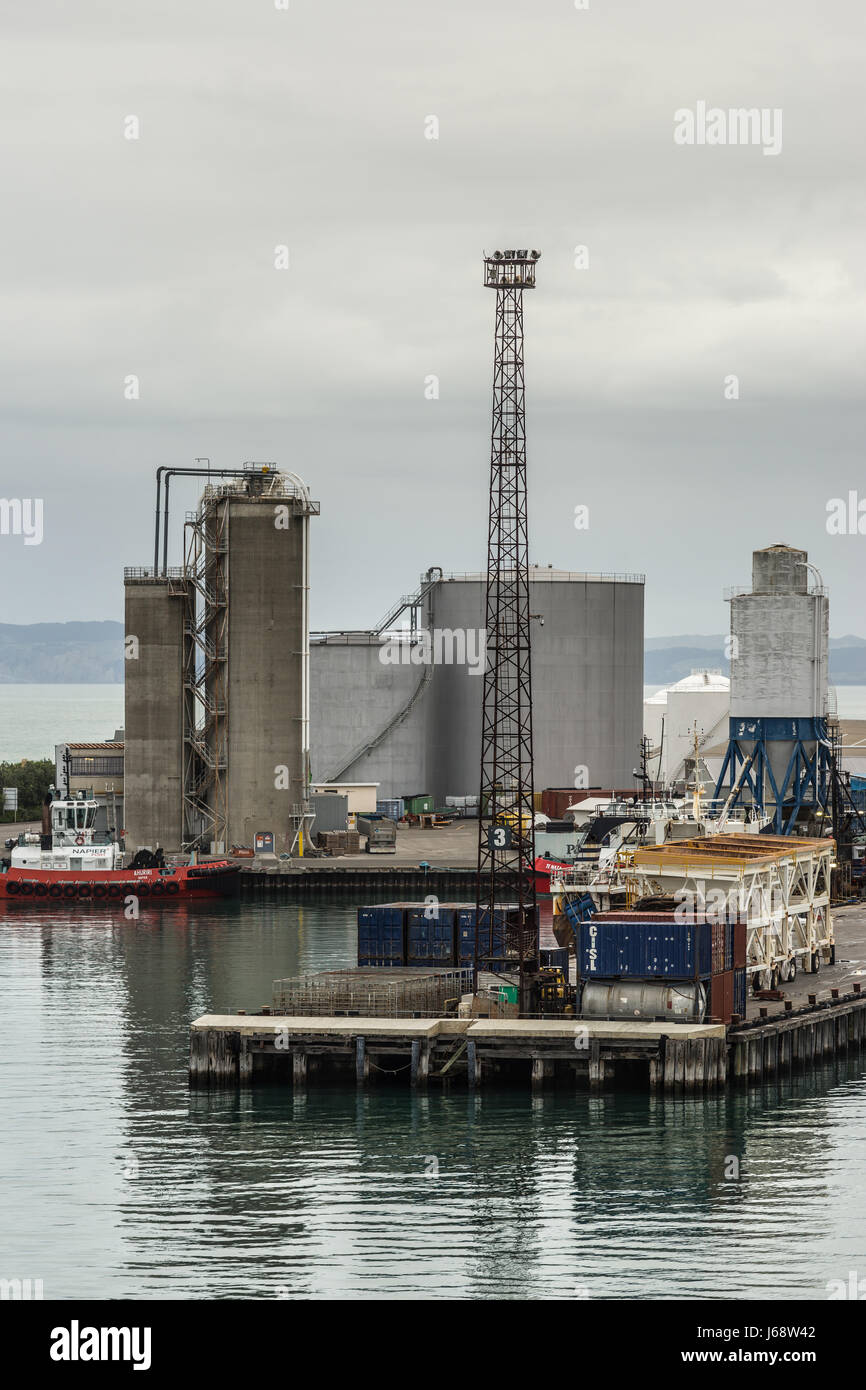Napier, New Zealand - March 9, 2017: Large fuel tanks and silos at the commercial port under silver sky. Tugboat, light poles, containers and other ha Stock Photo