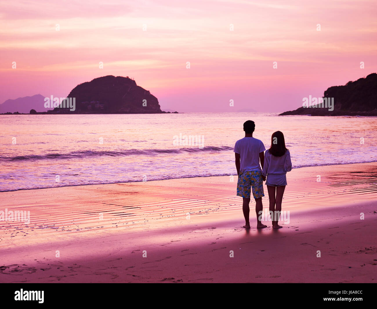 young asian couple taking a walk on beautiful beach before sunrise. Stock Photo