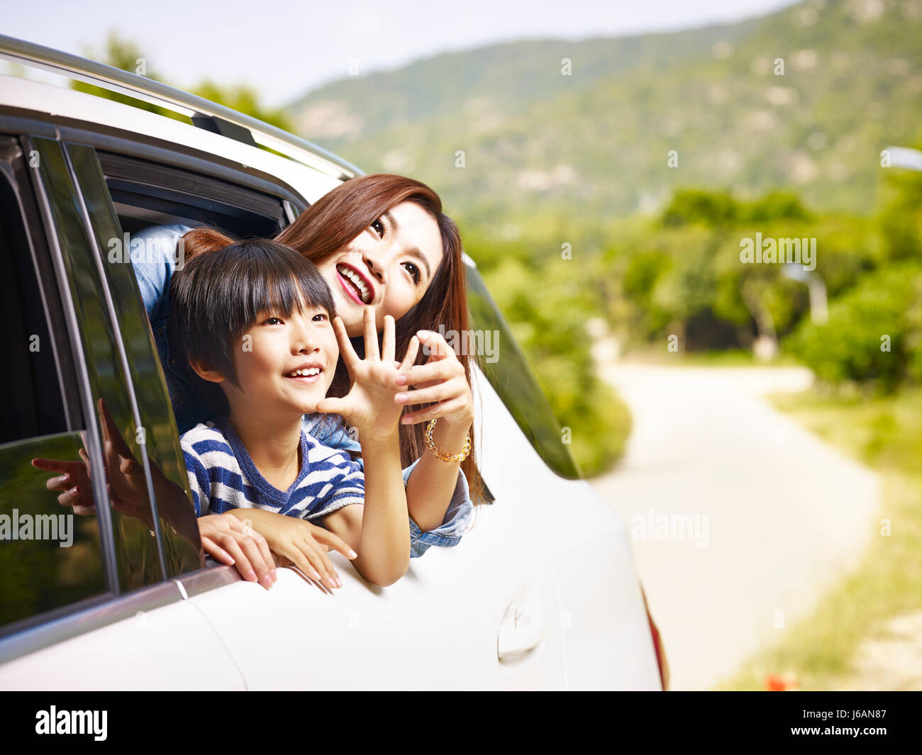happy asian mother and son sticking heads out of rear window of a car looking at scenery. Stock Photo