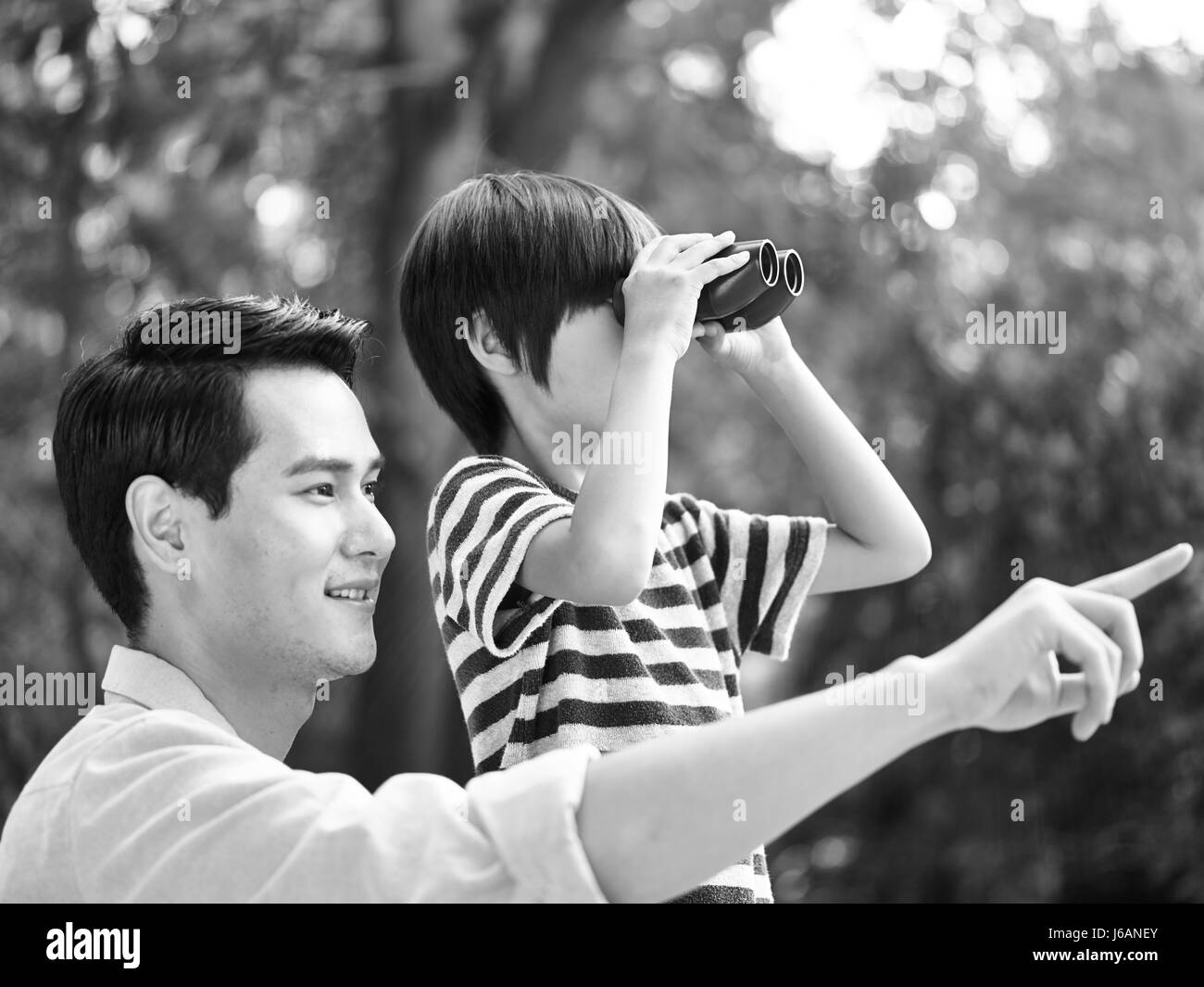 asian father and son using binoculars in park, black and white. Stock Photo