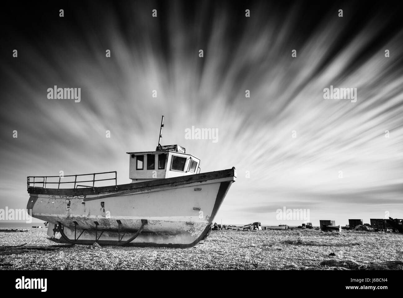 Abandoned old fishing boat on a pebble beach with long exposure clouds in monochrome. Dungeness, England Stock Photo