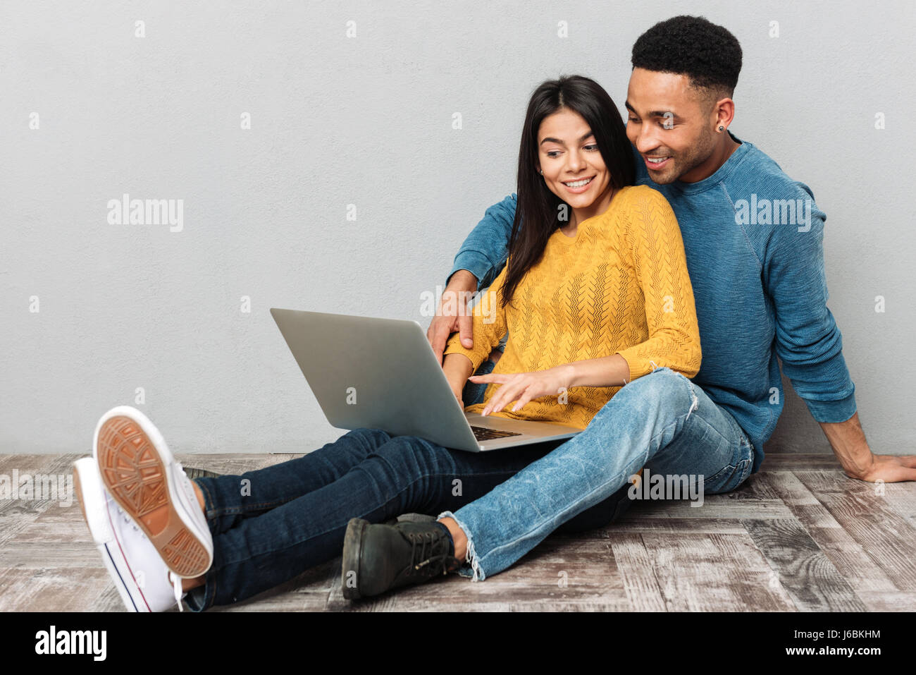 Pretty smiling couple using laptop sitting on floor isolated Stock ...