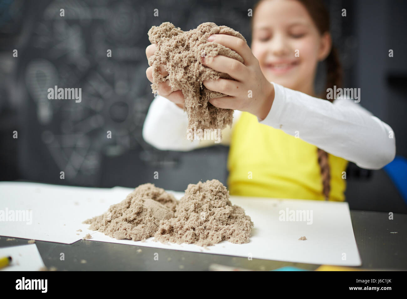 Portrait of cute little girl enjoying play with kinetic sand in daycare center, smiling happily Stock Photo