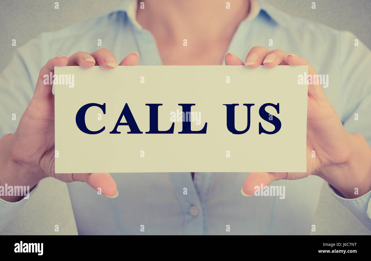 Closeup retro image silhouette businesswoman, female hands holding white sign or card with message call us customer support isolated on gray office wa Stock Photo