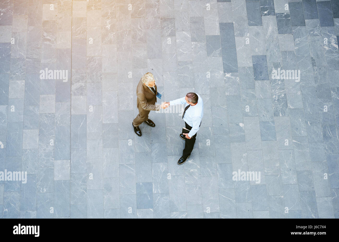 From above adult male office workers standing in empty hall and handshaking. Stock Photo