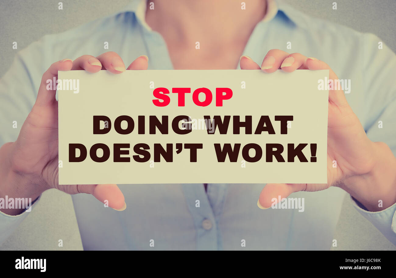 Businesswoman hands holding white card sign with Stop Doing What Doesn't Work text message isolated on grey wall office background. Retro instagram st Stock Photo