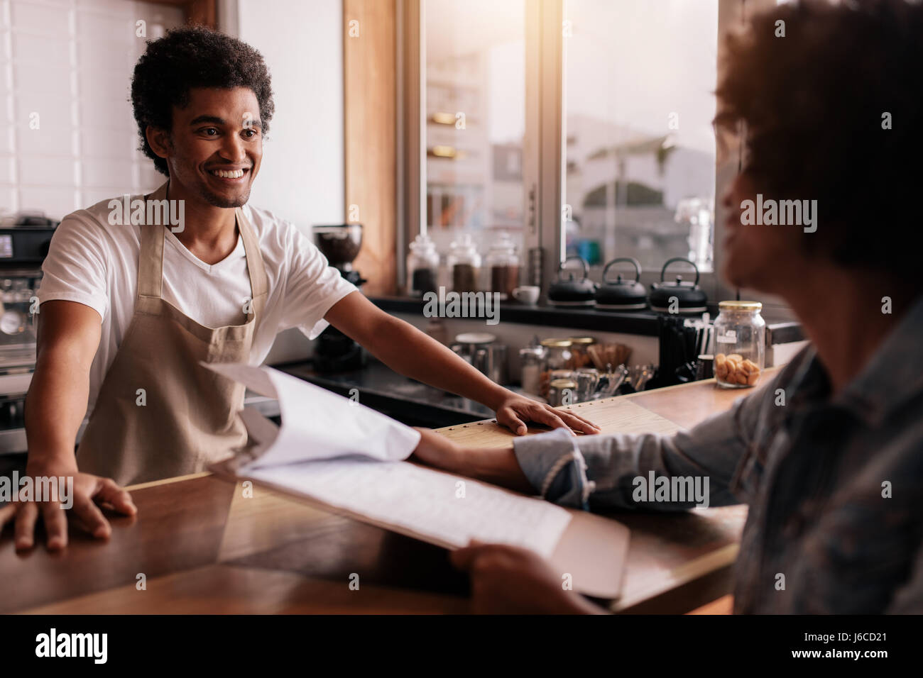 Young male barista taking an order from a female customer in a coffee shop and smiling Stock Photo